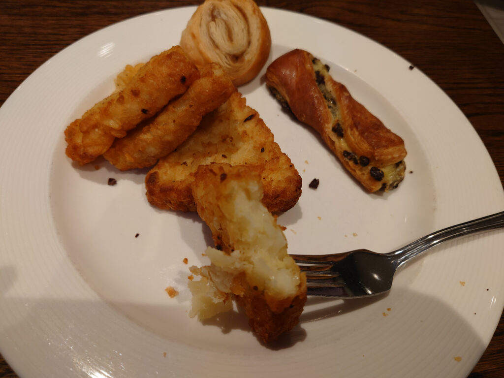 A photo of a plate with 3 small puff patries and four hash browns, with one on a fork and half eaten.