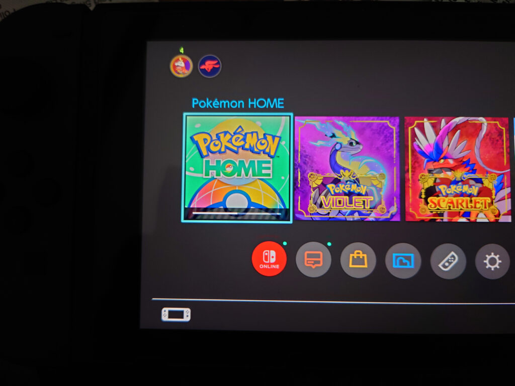 A photo of a Nintendo Switch showing the home screen. Pokémon HOME is selected and has a progress bar showing it's downloading and installing updates