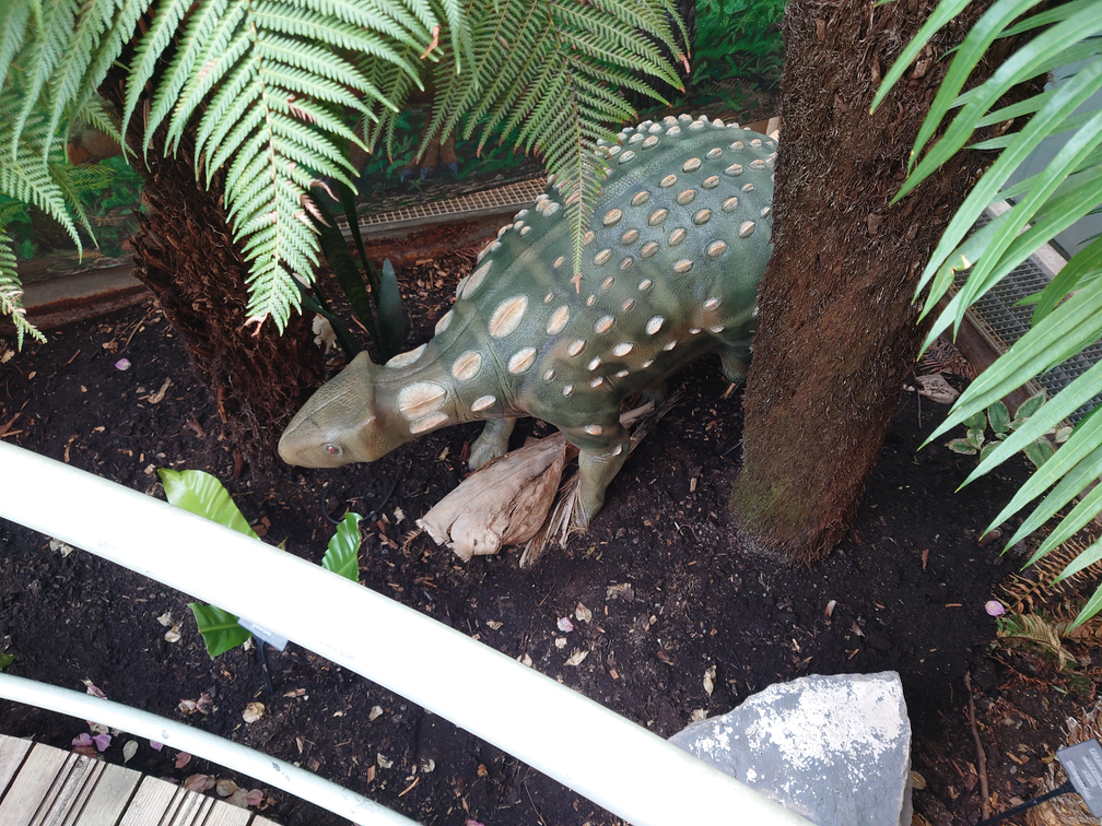 A photo of a tropical area in Bristol Aquarium. There is a dinosaur statue in the foliage