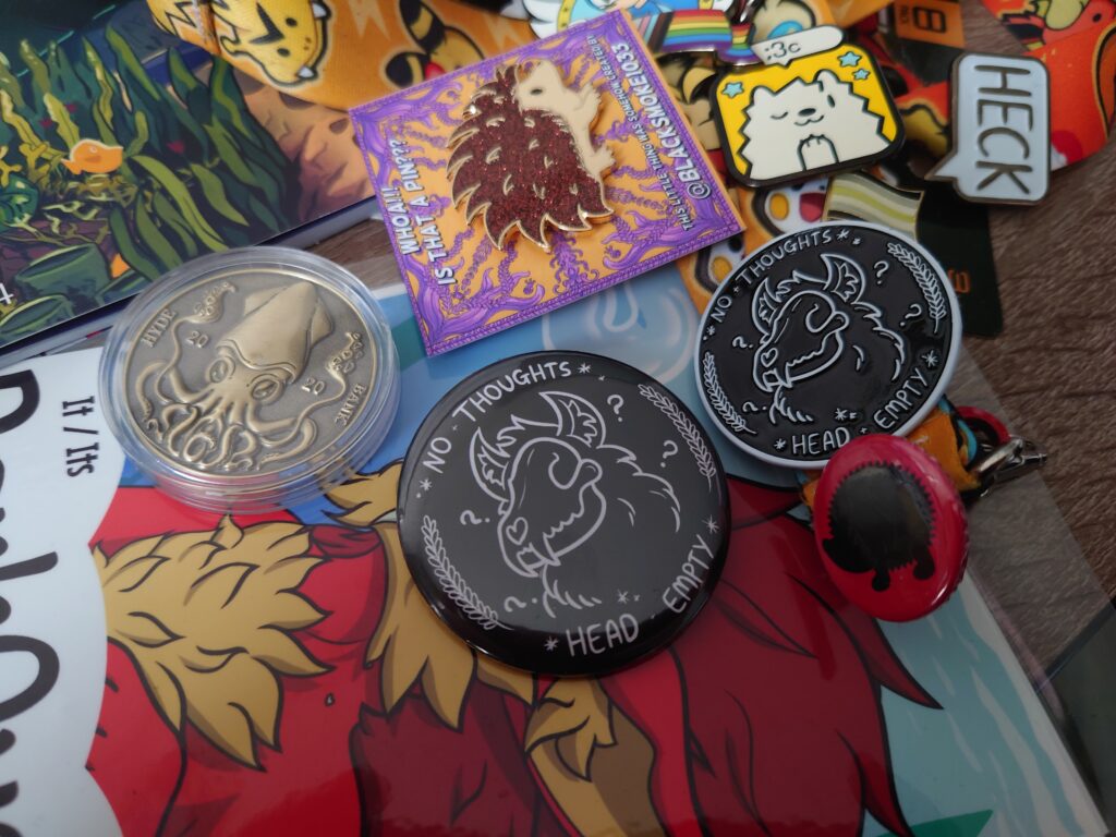 A photo of pins and a coin from BlackSmoke1033 featuring a "No thoughts, head empty" pin and a glittery hedgehog pin